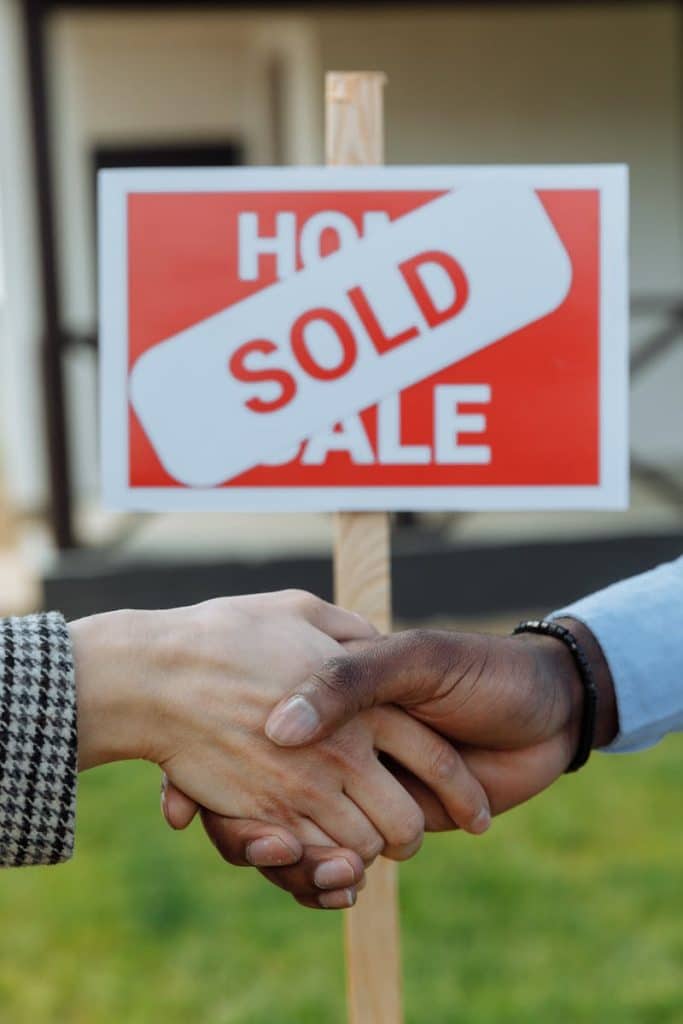 Close-up of a handshake in front of a sold sign symbolizing a successful real estate transaction.